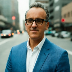 Carlos Flores, man standing on city street, wearing blue blazer, white button-down shirt and dark-rimmed glasses